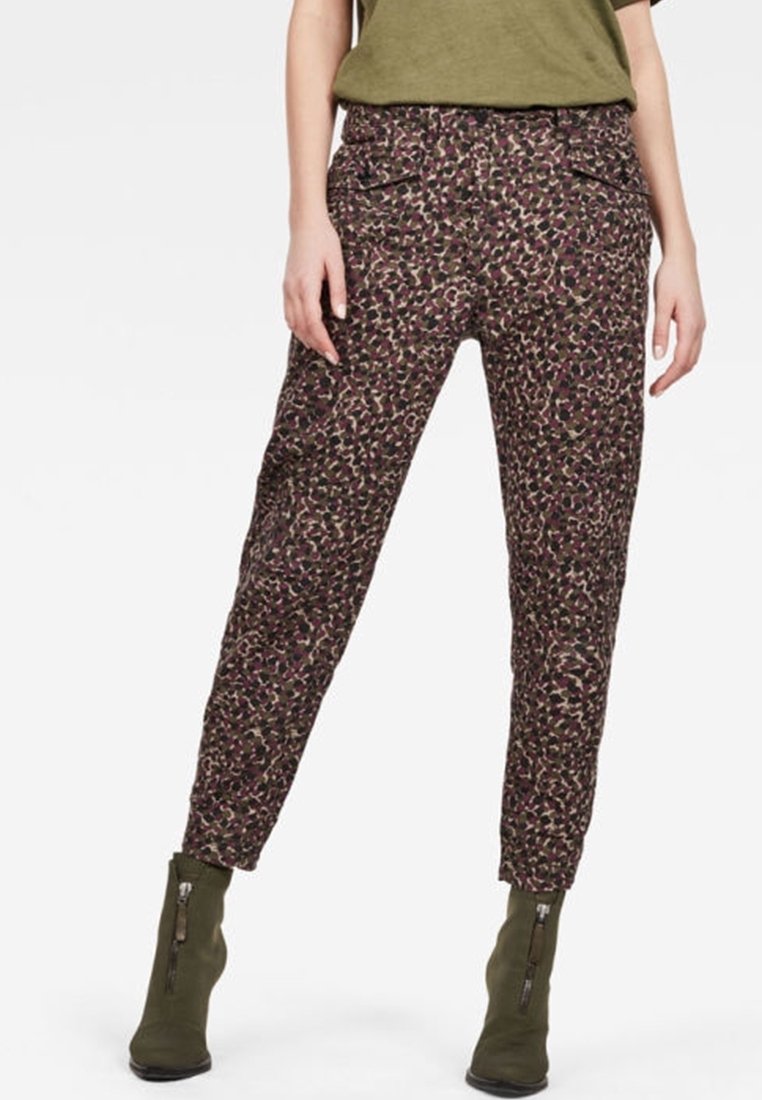 Pantalon fuselé à motifs dans des tons foncés, présentant un mélange de dessins floraux violets et verts, avec des poches latérales et des fermetures éclair aux chevilles.