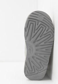 Szara gumowa podeszwa z zygzakowym wzorem bieżnika i logo UGG. Gładka, teksturowana powierzchnia wzdłuż krawędzi, zaprojektowana z myślą o przyczepności i trwałości.