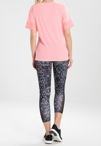 Jasnoróżowa koszulka sportowa z krótkim rękawem, w połączeniu z czarnymi i szarymi legginsami w wzory z siateczkowymi akcentami. Czarne trampki.