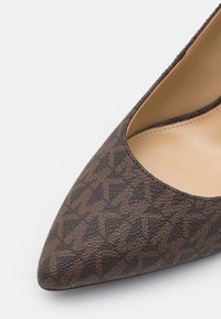 Scarpa con tacco alto di colore marrone, decorata con un motivo e con punta affilata e superficie testurizzata. L'interno presenta una fodera liscia beige.