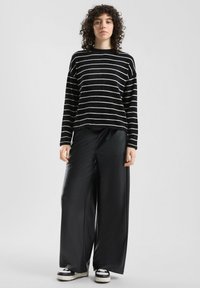 Czarnobiały sweter w paski ze szerokimi rękawami, w połączeniu z wysokim stanem czarnych spodni z szerokimi nogawkami ze sztucznej skóry oraz czarnymi sneakersami.