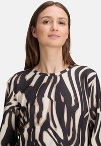 Langermige top met een zwart en beige abstract dierenprint, ronde halslijn, geribbelde textuur en zachte, gebreide stof.