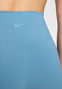 Jasnoniebieskie legginsy sportowe wykonane z gładkiego, elastycznego materiału. Charakteryzują się wysokim pasem i małym logo Nike z tyłu.