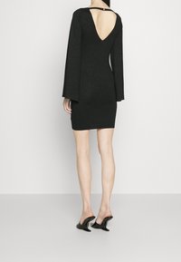Robe mini noire scintillante avec de longues manches évasées et un dos en V profond. Associée à des mules noires brillantes.