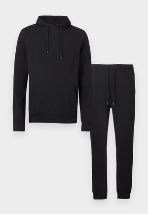 Hoodie noir avec poche avant et cordons ajustables, associée à un pantalon de jogging noir avec cordons à la taille et chevilles resserrées.