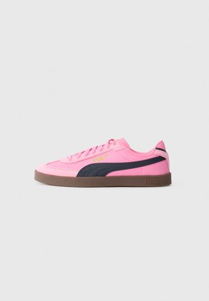 Låg sneakers i rosa med svart Puma-remsa, brun sula, guld Puma-logotyp på sidan och rosa snören, uppställd på vit bakgrund.