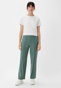 White short-sleeve t-shirt paired with high-waisted, green wide-leg trousers made of smooth fabric. White sneakers complete the outfit.