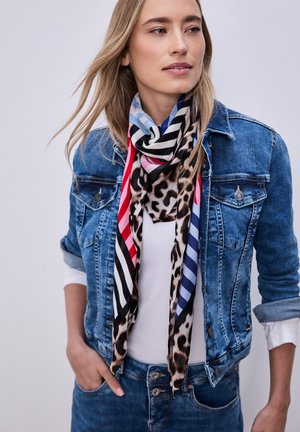 Blonde vrouw die een spijkerjasje draagt over een wit shirt, met als accessoire een sjaal met meerkleurige strepen en luipaardprint.