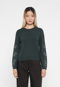 Pull en tricot vert foncé avec un col rond, décoré de broderies florales blanches sur les manches et de bords-côtes aux poignets et à l'ourlet.