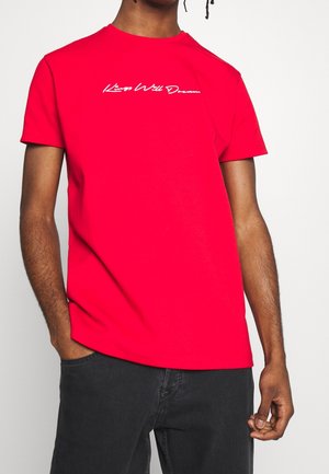 T-shirt rouge à manches courtes en coton, arborant un logo en cursive blanc "Kings Will Dream" sur la poitrine, un col rond et une coupe décontractée.