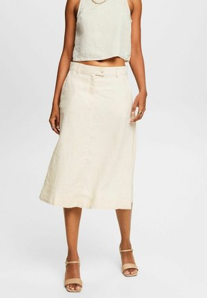 Mujer que lleva una camiseta sin mangas recortada de color blanco roto, falda midi de talle alto, collar de cadena dorada, anillos y tacones abiertos beige.