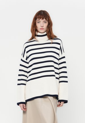 Maglione a collo alto a righe in crema e blu navy. Presenta una vestibilità rilassata, una texture a coste e maniche larghe, con un orlo leggermente asimmetrico.