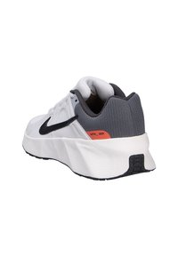 Zapatilla deportiva blanca con un swoosh negro, talón texturizado gris y un acento naranja. Presenta una suela acolchada y parte superior de malla transpirable.