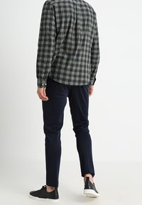 Harmaa-musta ruudullinen paita, pitkät hihat, napitetut kalvosimet, yhdistetty tummansinisiin housuihin. Mustat lenkkarit valkoisilla pohjilla, sileä pinta.