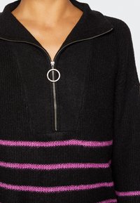 Schwarzer Reißverschluss-Pullover mit Kragen, der horizontale rosa Streifen aufweist. Aus strukturiertem Strickstoff gefertigt, mit silbernem Reißverschluss und Ringen als Akzent.