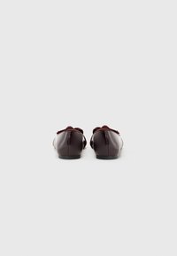 Mocassins en cuir verni bordeaux avec une semelle plate, un bout arrondi et un accent en nœud à l'avant. Texture lisse et design minimaliste.