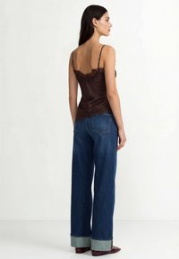 Rjava satenska majica s čipkastim robom, kombinirana z ohlapnimi modrimi jeans hlačami z zavihanimi robovi. Model prikazan od zadaj.