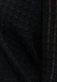 Μαύρο ύφασμα με σχέδιο πλέξης σχήματος σβώλου, ελαφρώς διαφανές με ορατή υφή και σκιερές πτυχώσεις.