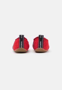 Chaussons en feutre rouge au toucher doux, avec une marque noire au niveau du talon et une semelle en caoutchouc beige pour une adhérence et une durabilité accrues.