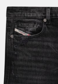 Jeans in denim nero con dettagli consumati, dotati di tasca frontale e etichetta del marchio visibile, completati da accessori in metallo.