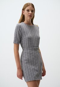 Abito in tweed bianco e nero con maniche corte, vita aderente e due bottoni dorati decorativi su una spalla e lungo la parte anteriore.