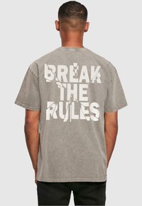 Grijze oversized t-shirt met grote witte tekst "BREAK THE RULES" met een versleten uitstraling op de achterkant. Zacht katoenen materiaal, korte mouwen.