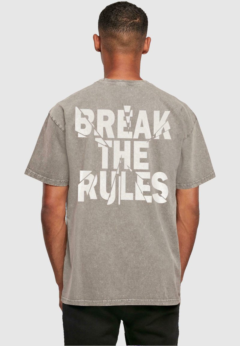 Grijze oversized t-shirt met grote witte tekst "BREAK THE RULES" met een versleten uitstraling op de achterkant. Zacht katoenen materiaal, korte mouwen.