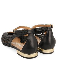 Sandales tissées noires avec une sangle réglable, des accents en cuir et un détail de talon doré. La semelle intérieure présente un design beige.
