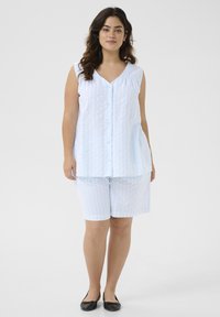 Haut sans manches à rayures bleu clair avec des boutons et un short assorti. Le tissu a une texture douce. Des chaussures plates noires complètent l'ensemble.