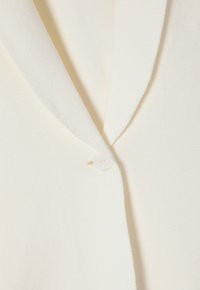 Cardigan color crema con una texture morbida, caratterizzato da un collo a rever e una chiusura con un singolo bottone bianco.
