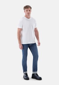 Weißes Baumwoll-T-Shirt mit kurzen Ärmeln, kombiniert mit blauen Jeans, hochgerollten Bündchen und schwarzen Lederschuhen mit dicker Sohle.