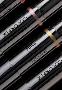 Vier glanzende, cilindrische pigmentsticks met metalen doppen en gekleurde ringen: brons, goud en een zwarte label met de tekst "FOILS MULTI-USAGES."