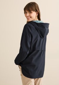 Chaqueta de lluvia azul marino con capucha, con un forro azul claro y un bolsillo con cremallera en el lado. Material exterior texturizado.