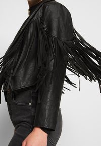 Czarna kurtka z eko skóry z długimi, zwiewnymi frędzlami, krótkim krojem i zamkiem błyskawicznym. Posiada ściągacze na mankietach oraz ozdobne detale na ramionach.