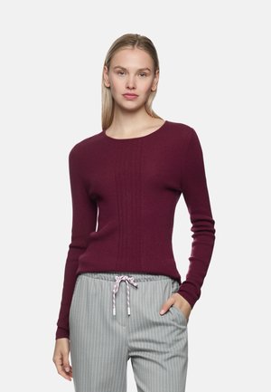 Bordeauxroter, gerippter Pullover mit langen Ärmeln und rundem Ausschnitt, kombiniert mit grauen Nadelstreifenhosen mit verstellbarem Kordelzug.