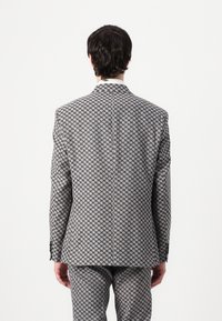  Skräddarsydd kostym med houndstooth-mönster i svart och vitt. Har en strukturerad design, spetsig slag och skräddarsydd passform. Bakifrån visad.