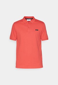 Polo rouge à manches courtes avec col, patte à deux boutons et petit patch logo noir Calvin Klein sur la poitrine gauche.