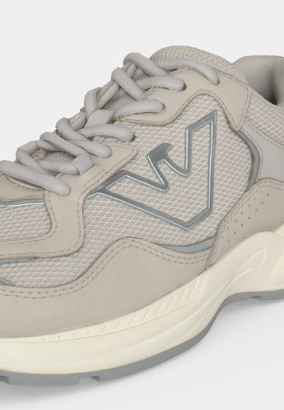 Chaussure de sport gris clair en tissu mesh, détails en daim et un logo argenté en zigzag sur le côté, avec une semelle épaisse et rembourrée et des lacets.