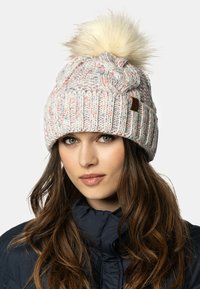 Strikket hue i lyserød med multicolorede sprøjt, har en fluffy hvid pom-pom på toppen og et struktureret ribbet bånd.