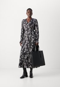 Duga crna haljina na preklop s bijelim cvjetnim uzorkom, zategnuta u struku. Modelira crnu kožnu torbu i čizme do koljena u crnoj boji. Glatka tekstura.