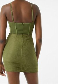 Zeleno-olivové mini šaty s přiléhavým střihem, jemnými ramínky a texturovanou látkou s jemným vlnitým vzorem.