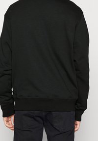 Svart sweatshirt med en mjuk textur, ribbstickade muddar och fåll, samt en enkel design utan synliga logotyper eller mönster.