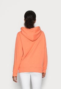 Felpa corallo con grande cappuccio, polsini e orlo a coste. Texture morbida e vestibilità ampia. La vista posteriore mostra cuciture e dettagli delle cuciture.