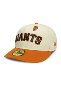Gorra cremosa con visera naranja, con el bordado "GIANTS" en marrón y un parche del logo. Diseño estructurado, visera curvada, etiqueta de New Era visible.
