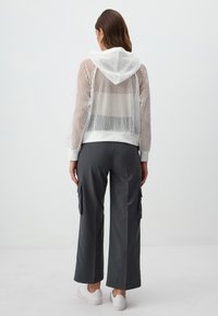 Hoodie bianco in rete con orlo aderente e cappuccio, abbinato a pantaloni cargo larghi grigi scuri con tasche laterali e sneakers bianche.