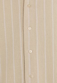Maglia beige lavorata a maglia con strisce verticali bianche, caratterizzata da quattro bottoni rotondi crema lungo il davanti e tessuto texturizzato.