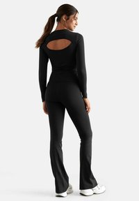 Black athletic outfit featuring a long-sleeved top with an open back detail and flared pants. Made from stretchy fabric for comfort.