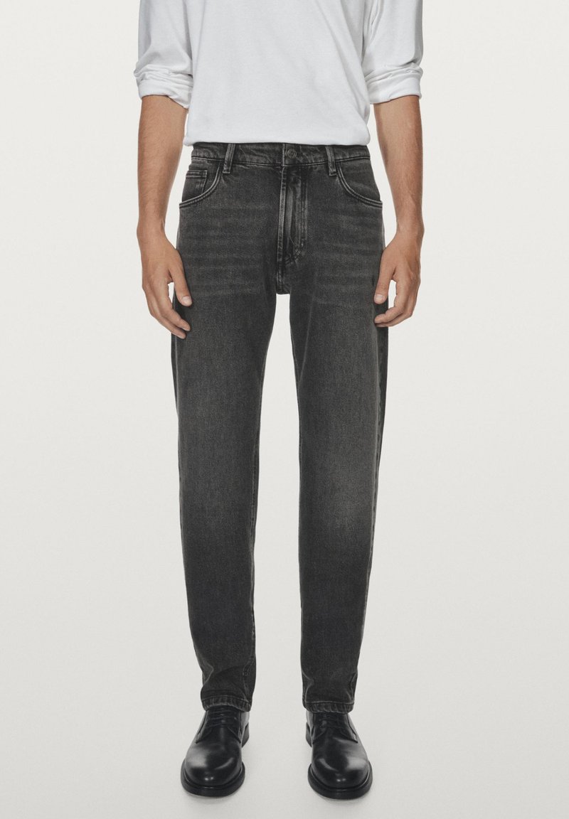 Jean en denim gris foncé avec une coupe droite et un design classique à cinq poches. Présente un léger délavage et des accents cousus, porté avec des chaussures noires.