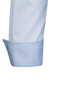 Polsino di camicia azzurro chiaro con superficie testurizzata e piccoli punti blu. L'interno del polsino presenta un motivo a pois coordinato.