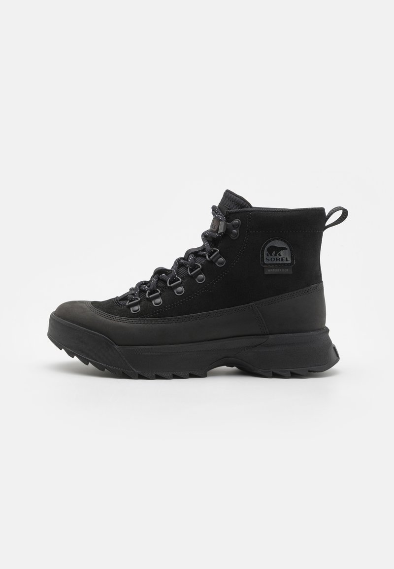 Zwarte waterdichte wandelen schoenen gemaakt van suede en rubber. Kenmerken zijn een hoge schacht, uitstekende veters en een gestructureerde zool.